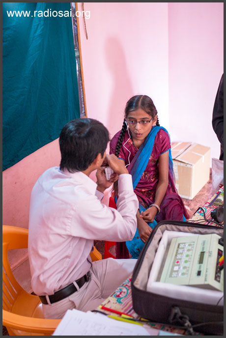 doctor testing hearing aid with partially deaf indian girl at mobile hospital portrait
